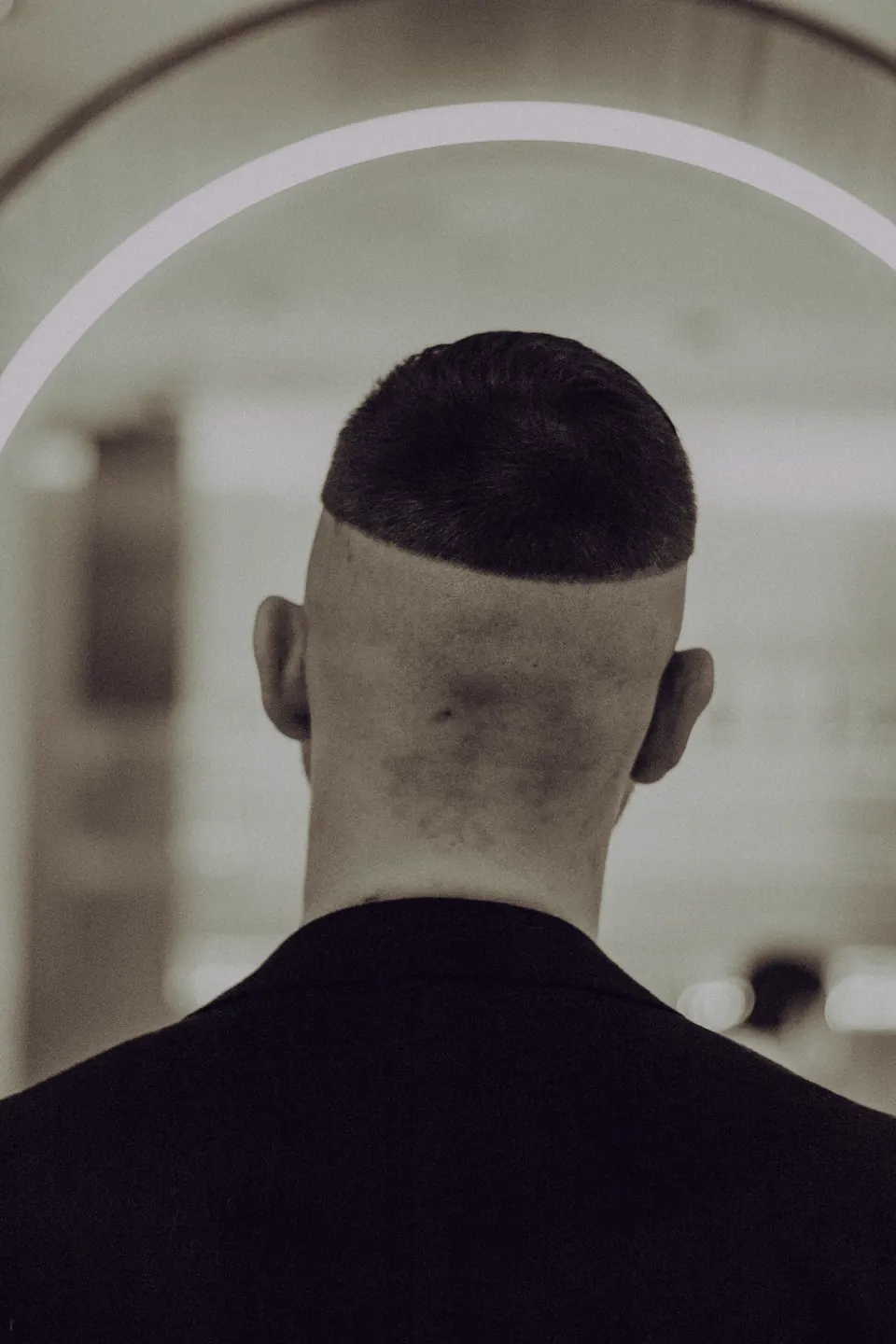 Rückansicht: sauberer Skin Fade vor einem hellen Rundbogen