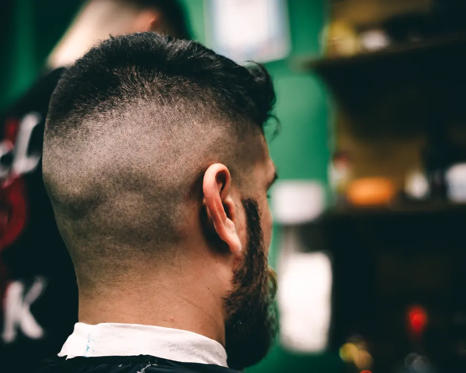 Hinterkopf mit sauberem Fade und Bartansatz vor grün verschwommenem Hintergrund