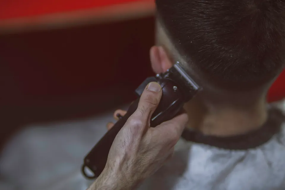 Clipper am Hinterkopf, Nahaufnahme vor dunkelrotem, unscharfem Hintergrund