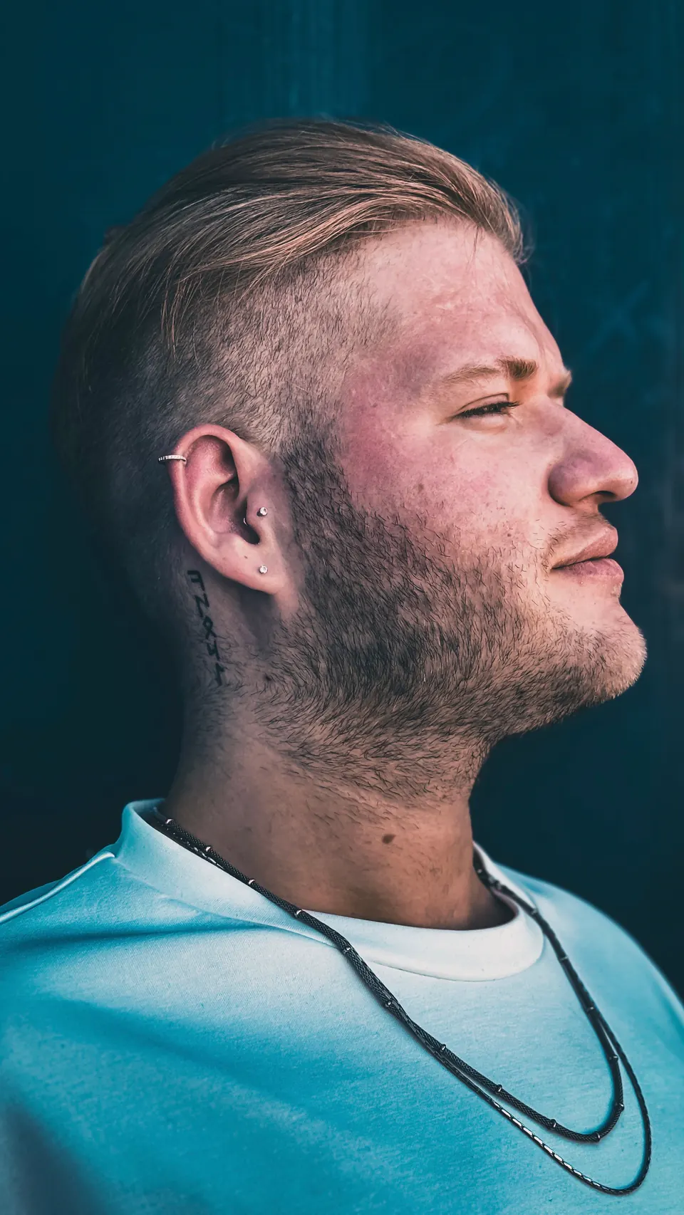 Profil eines Mannes mit Undercut und zurückgekämmtem Deckhaar vor petrolfarbenem Hintergrund