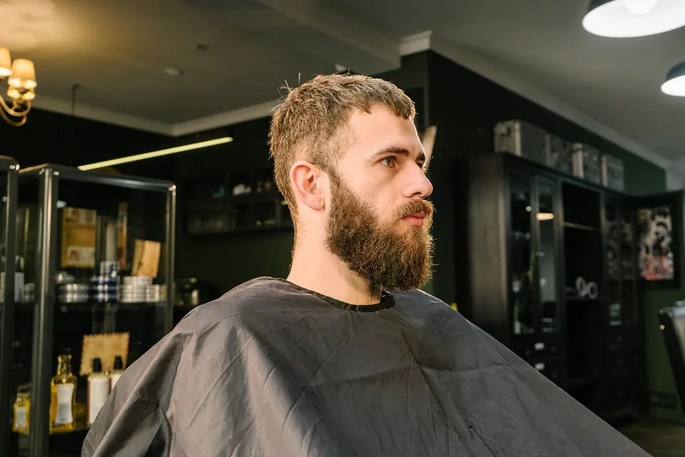 Ein Mann mit gepflegtem Vollbart im Umhang in einem dunklen Barbershop