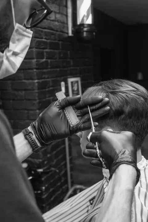 Schwarzweißaufnahme: ein Barbier mit Handschuhen arbeitet vor einer Backsteinwand